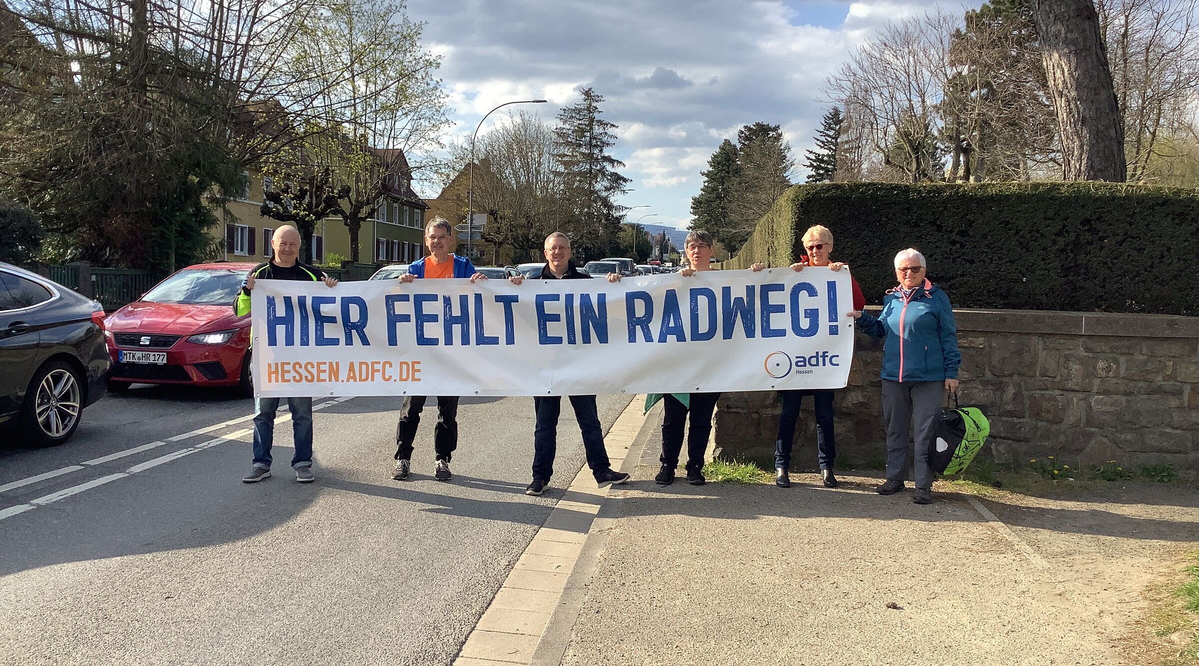 Personengruppe hält Banner hoch "Hier fehlt ein RAdweg"