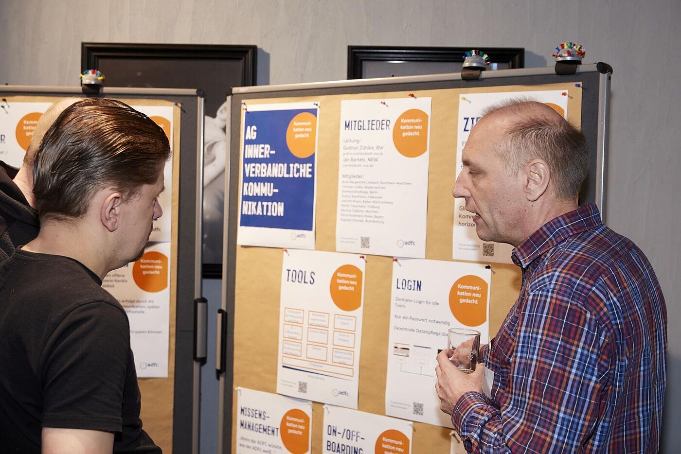 Zwei Männer unterhalten sich vor Pinnwänden mit Informationsplakaten.