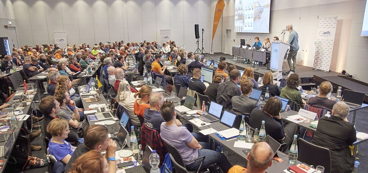 Ein grpßer Saal mit 140 Menschen an Tischreihen, die zur Bühne blicken, wo Boris von Heesen einen Vortrag hält. 