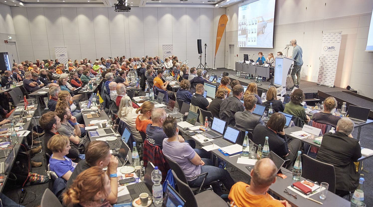 Ein grpßer Saal mit 140 Menschen an Tischreihen, die zur Bühne blicken, wo Boris von Heesen einen Vortrag hält. 